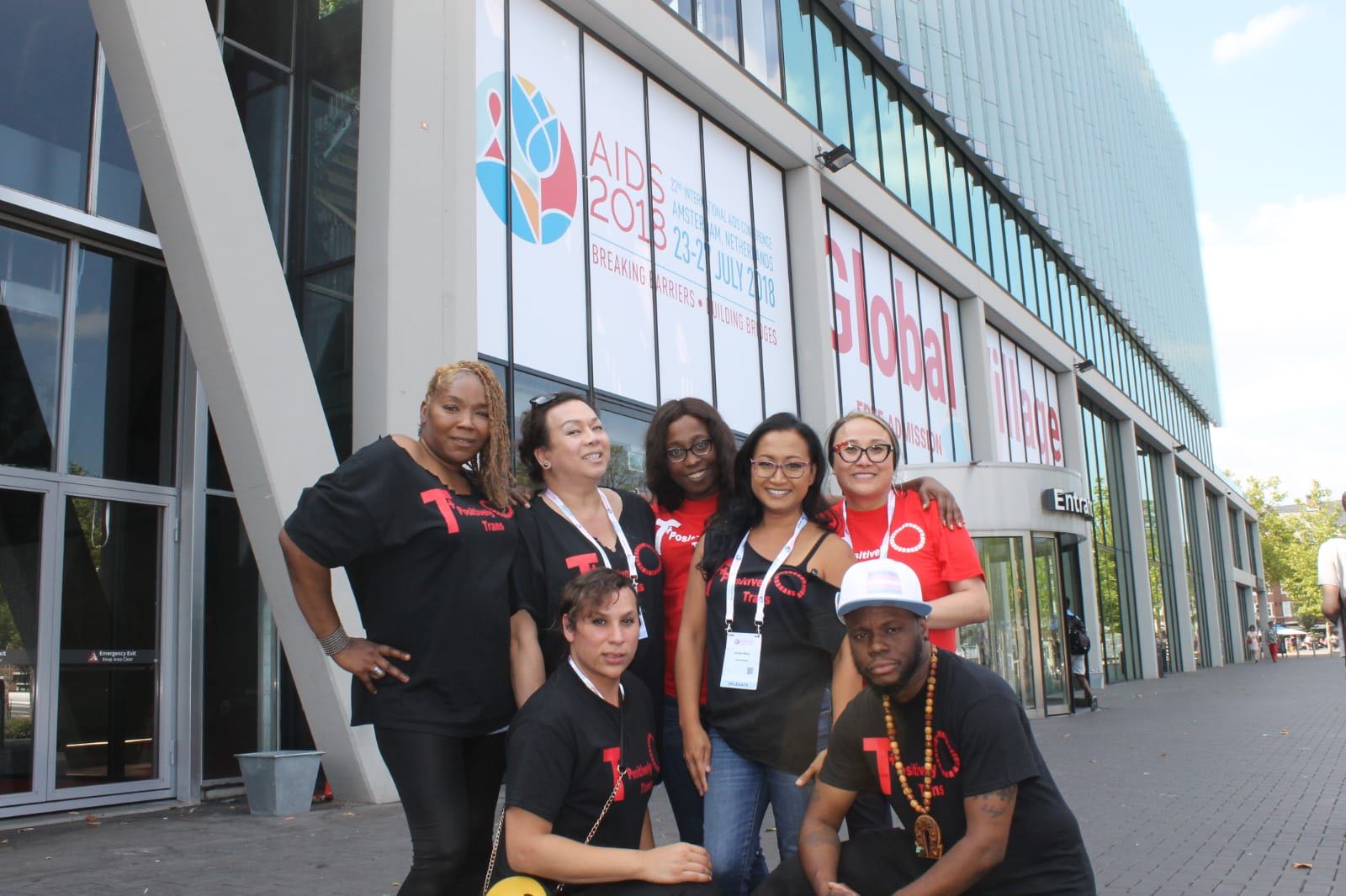 US trans advocates of color pose in front of conference center with AIDS 2018 banner