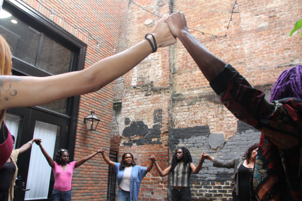 People standing in a circle holding hands, raised in the air.
