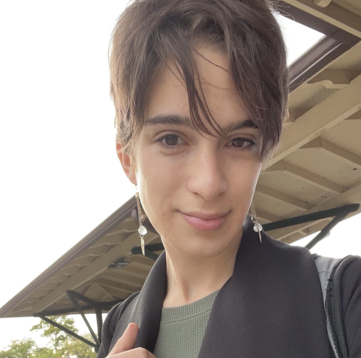 Arielle Rebekah, a white trans feminine person with short brown hair, pictured from the chest-up and wearing a black coat and green dress.