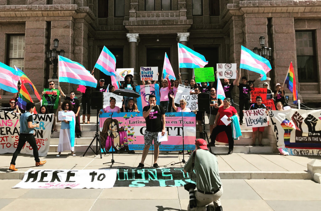 LGBTQ+ Protest. A group of people standing in front of a building with signs and flags.