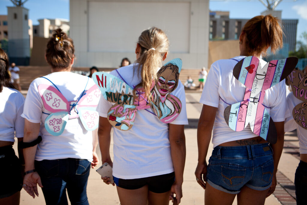Feminine people standing next to each other, all of them are wearing pink and blue butterfly wings on their backs.
