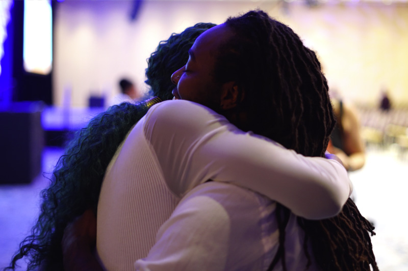Two Black, feminine people, who are embracing each other in a loving hug.