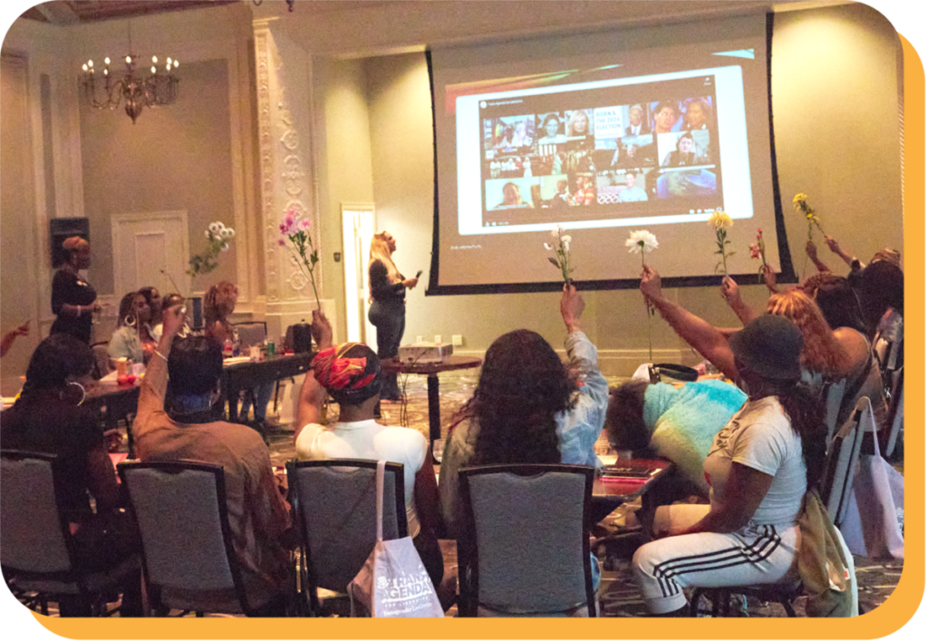 Conference room and Zoom screen full of Black trans activists holding single flowers high, celebrating their power.