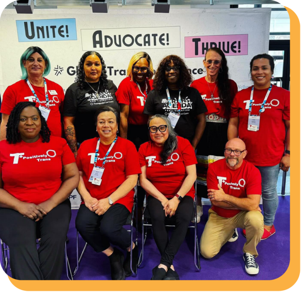A group of diverse activists wearing red “T+ Positively Trans” t-shirts pose in front of conference signage in blue, pink, and white with the words “Unite! Advocate! Thrive!”